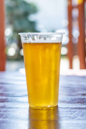 beer in a plastic mug on a brown table with a blurry backgroundの写真素材