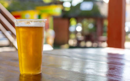 beer in a plastic mug on a brown table with a blurry backgroundの写真素材