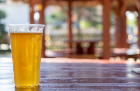 beer in a plastic mug on a brown table with a blurry backgroundの写真素材