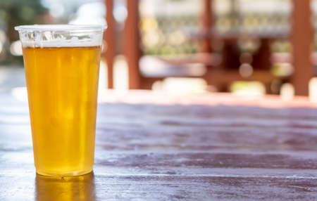 beer in a plastic mug on a brown table with a blurry backgroundの写真素材