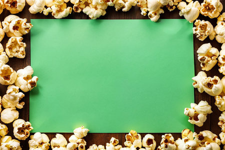 Popcorn and green paper on wooden background. Top view with copy space. AI generatedの素材