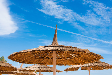 straw beach umbrellas on blue sky backgroundの写真素材
