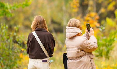 Two girls are photographing an autumn landscape with a phoneの写真素材