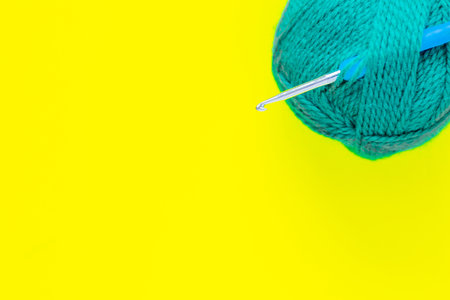 A metal hook with a blue handle is inserted into a skein of green yarn in the upper corner of the photo on a yellow background. top view, flat lay, copy space, isolate.の写真素材