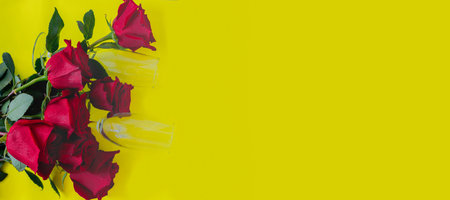 A bouquet of beautiful red roses and two champagne glasses are lying on the side on a yellow background. top view, flat lay, copy space, isolate.の写真素材