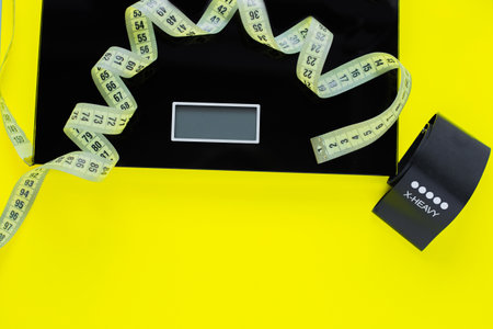A weight scale, a black fitness tape and a yellow measuring tape lie on a yellow background on top of the photo. top view, flat lay, copy space, isolate.の写真素材