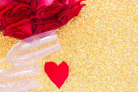 Two champagne glasses, a red bouquet of roses and a heart of petals lies on the side on a bright gold background. top view, flat lay, copy space, isolate.の写真素材