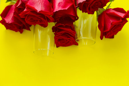 A bouquet of beautiful red roses and two champagne glasses are lying on the side on a yellow background. top view, flat lay, copy space, isolate.の写真素材