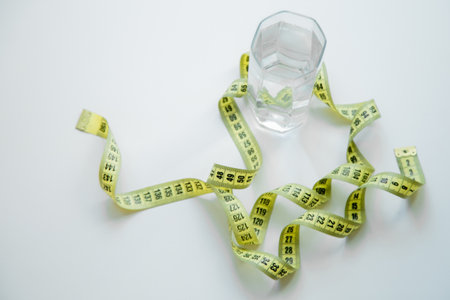 A glass of water is wrapped with a measuring tape on a white background. . High quality photoの写真素材