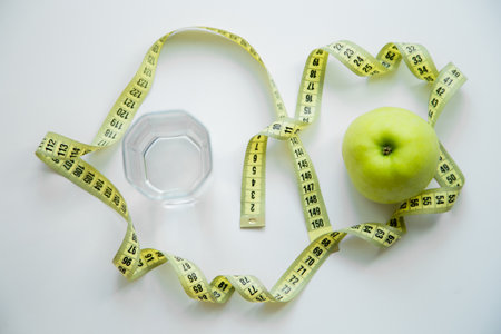 A green apple and a glass of water stand on a white background, they are entwined with a measuring tape. High quality photoの写真素材