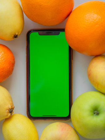 A phone with a green screen is lying among the fruits. High quality photoの写真素材