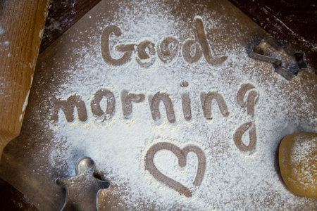 On the baking paper on the flour is written Good morning and heart, against the background of dough, rolling pins and cookie cutters. High quality photoの写真素材