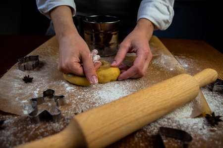 In the foreground is a table with baking parchment lying on it, on which there is dough that the cook's hands are crumpling, a rolling pin, baking molds and flour are scattered around. High quality photoの写真素材