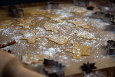 There are ready-made cookies of different shapes on the parchment, a rolling pin, cookie cutters and a sieve with flour are lying nearby, flour is scattered everywhere. High quality photoの写真素材