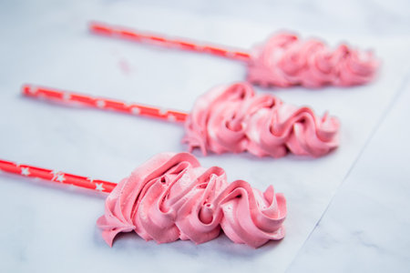 Pink meringue Christmas trees lie on baking paper, the front Christmas tree is in focus, the rest...