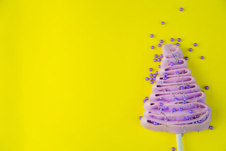 Pale purple Christmas tree made of meringue on a stick, decorated with purple and silver balls on a bright yellow background, purple powder balls are scattered near the tree. High quality photoの写真素材