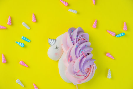 A white meringue unicorn with a pink-purple tail and a silver horn lies on a bright yellow background, with multicolored horns scattered around it. High quality photoの写真素材