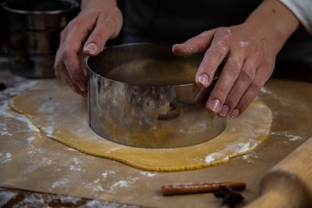 The rolled out layer of dough lies on baking paper, a cake cake is cut out of it with a metal...