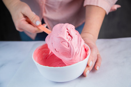 Pink confectionary meringue marengo is mixed in a white bowl on a white marble background by the hands of a pastry chef. High quality photoの写真素材