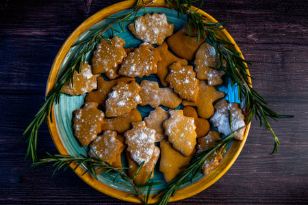 Cookies in the form of Christmas trees lie on a blue plate, decorated with rosemary on the sides on a dark background. High quality photoの写真素材