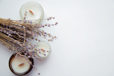 Several handmade aroma candles stand on the side on a white background, dry branches of lavender lie between them. High quality photoの写真素材