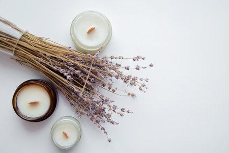 Several handmade aroma candles stand on the side on a white background, dry branches of lavender lie between them. High quality photoの写真素材
