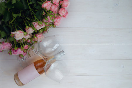 A large bouquet of pink roses and a bottle of rose wine with glasses lie on the side on a wooden white background with a place for text. High quality photoの写真素材