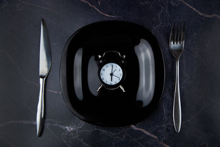 Inside the black plate is a black alarm clock, on the sides are devices on a dark background. High quality photoの写真素材