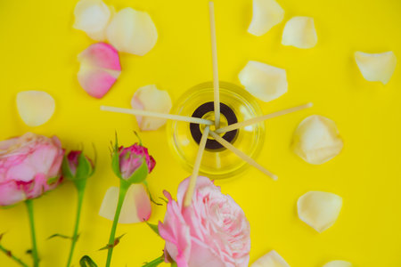 A glass jar with scented oil and wooden incense sticks in the room, next to roses and rose petals on...