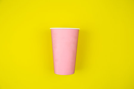 Paper cup for takeaway coffee pink color lies on a yellow background. High quality photoの写真素材
