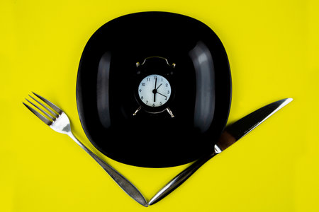 Inside the black plate is a black alarm clock, on the sides are devices on a yellow background. High quality photoの写真素材