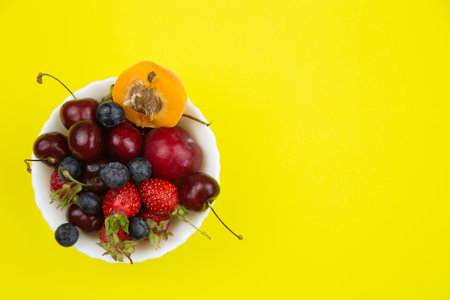 On a bright yellow background, there is a plate with fruits and berries on the side with a place for text, top view. High quality photoの写真素材