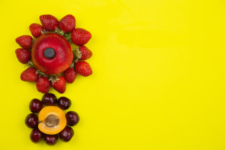 Creative flowers consisting of apricot and cherry and apple and strawberry lie on the side on a yellow background with space for text. High quality photoの写真素材