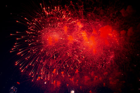 A bright firework with a red glowing center with red sparks and smoke flying towards the background of the night sky. High quality photoの写真素材