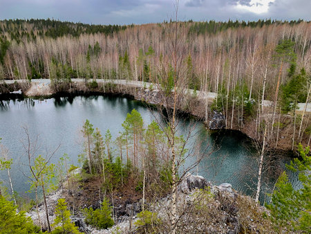 The lake is mountainous in the forest among the forest, bare trees and green pines are visible...