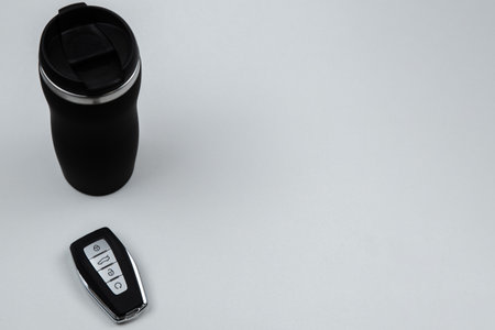 A thermocup and a key with automatic buttons in black and with metal inserts stand on a white background with space for text. High quality photoの写真素材