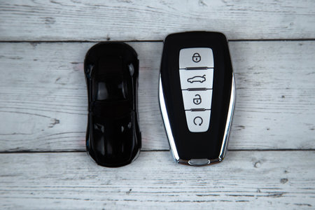 The car keys are black with metal inserts and automatic buttons lying on a white wood background,...