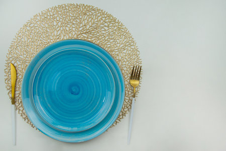 Bright blue serving plates stand on golden air-twisted napkins, on the sides are a golden knife and...