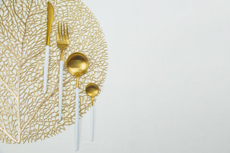 The food utensils, gold with a white handle, lie on a gold napkin on a white background. The concept of eating, the concept of serving. High quality photoの写真素材