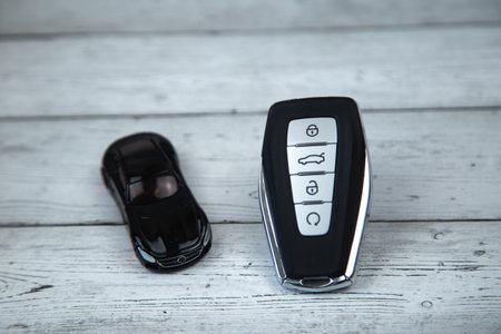 The car keys are black with metal inserts and automatic buttons on a background of white wood, next...