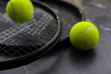 Against the background of dark marble, two tennis rackets lie one on top of the other, yellow tennis balls lie on them and next to them. The concept of sports and competitions. High quality photoの写真素材