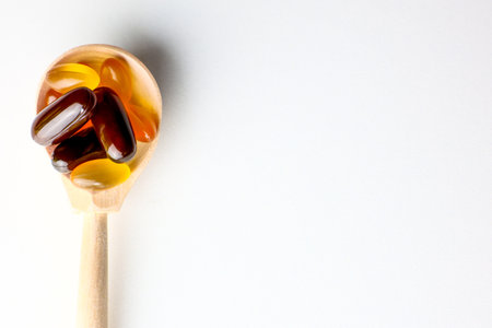 Yellow and red capsules with fats, vitamins and amino acids lying in a wooden spoon close-up on a white background. High quality photoの写真素材