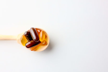 Yellow and red capsules with fats, vitamins and amino acids lying in a wooden spoon close-up on a white background with space for text. High quality photoの写真素材