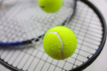 A yellow tennis ball lies against the background of two tennis rackets lying on top of each other on...