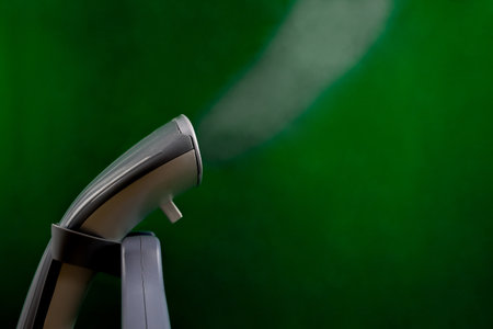 A gray and white steam generator stands close-up on a green background, a large stream of steam...