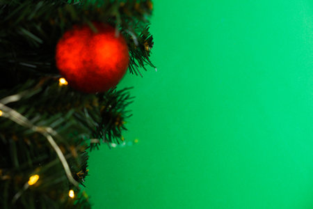 On the left there are branches of a Christmas tree with a red bright ball and a yellow glowing garland on a green background of a chroma key. Concept of Holiday, New Year Mood, New Year and Merry Christmas. High quality photoの写真素材