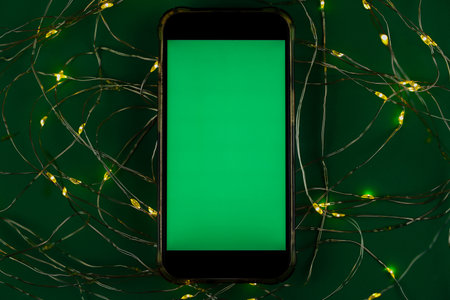 The phone lies horizontally with a green chromakey screen against a garland of yellow and green lights on a green background. High quality photoの写真素材
