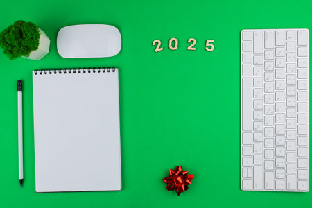 A white English computer keyboard flies to the right of the photo, on top are wooden numbers 2025, an office green plant and a white computer mouse, on the left lies a white notebook with a black spring and a white pencil with a black lead and a black eraser, at the bottom lies a bright red gift bow on a green chroma key background with space for text in the center. High quality photoの写真素材