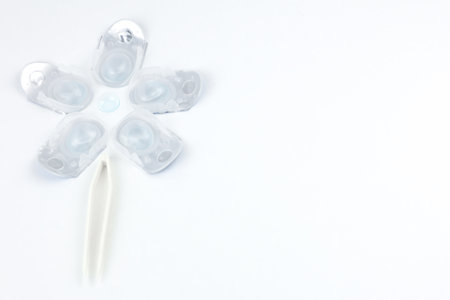Top and side view of a creative flower consisting of containers for daily contact lenses, in the center there is a soft bluish lens, down like the stem of a plant goes tweezers for taking lenses on a white background with space for text. High quality photoの写真素材