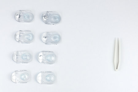 Disposable containers with contact lenses lie on the left in a few rows, on the right of the photo there are beige tweezers on a white background with space for text. High quality photoの写真素材